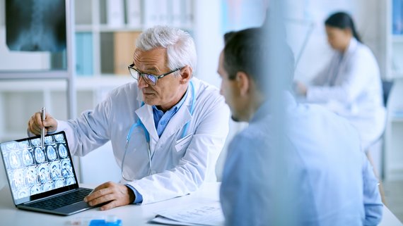 Arzt erklärt Patienten MRT-Aufnahmen am Notebook