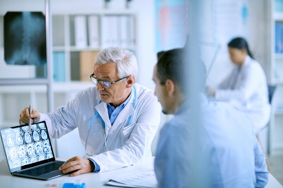 Arzt erklärt Patienten MRT-Aufnahmen am Notebook