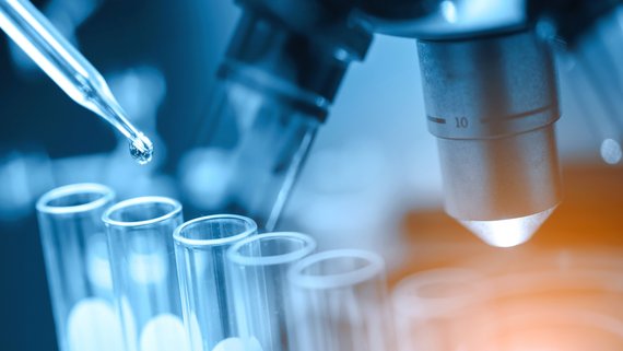 Pipette und Reagenzgläser vor einem Mikroskop